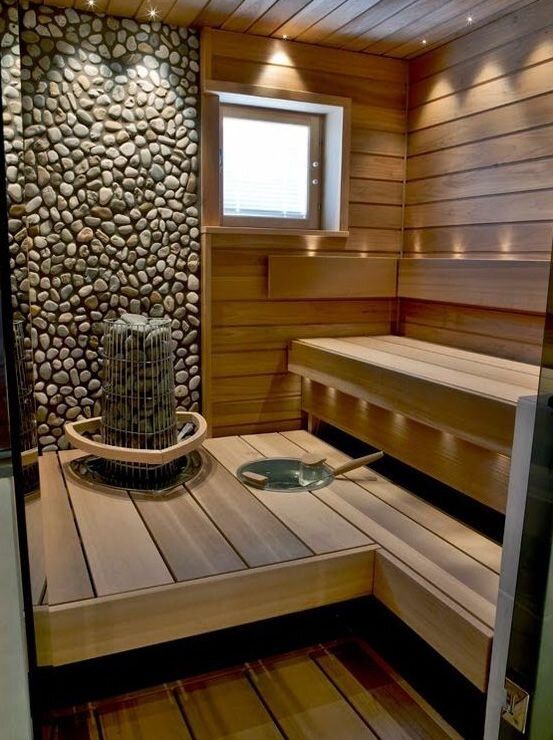 Modern wooden sauna interior with pebble wall and window, featuring benches and a central stone heater.