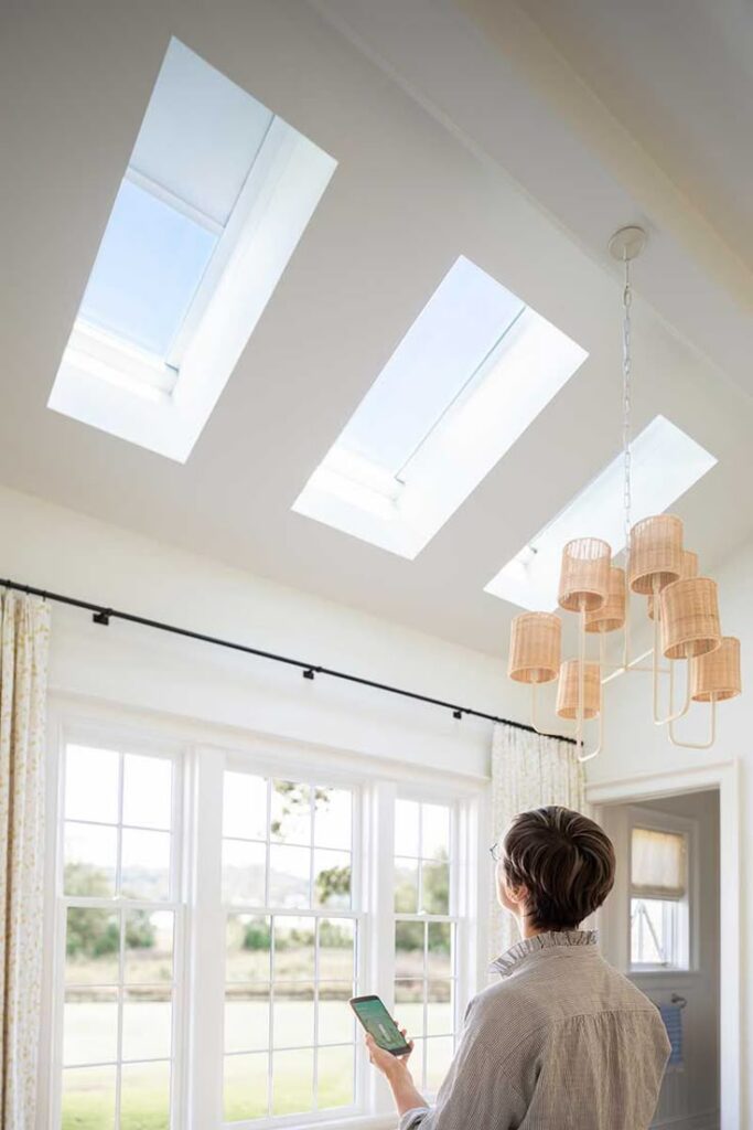 Person using smartphone to control skylights in a bright room with modern lighting.