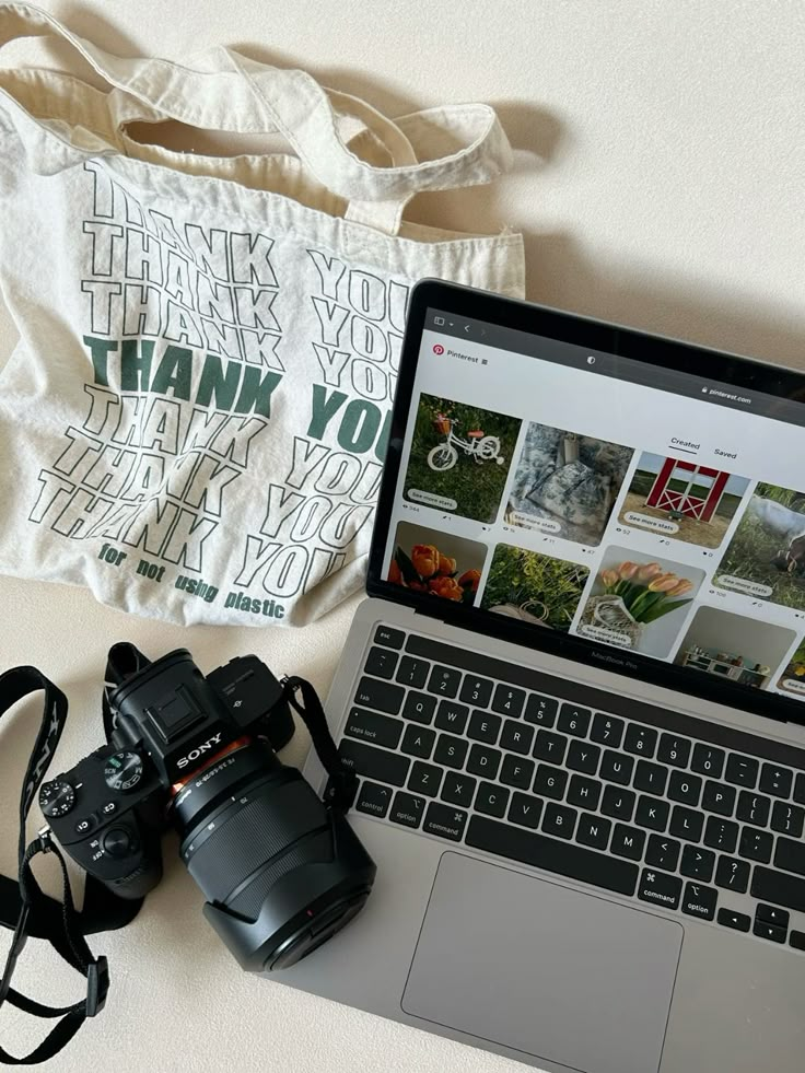 Eco-friendly tote, laptop with Pinterest, and Sony camera on a table, ideal for creative content creation.