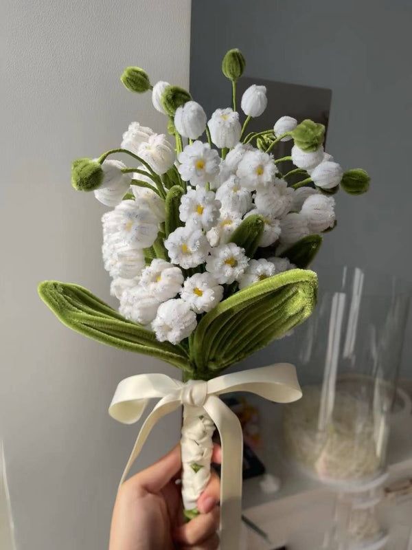 Hand holding a charming bouquet of white flowers with green leaves and a white ribbon tie, perfect for weddings.