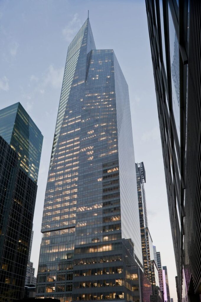 Tall modern skyscraper with glass facade in cityscape, captured at dusk.