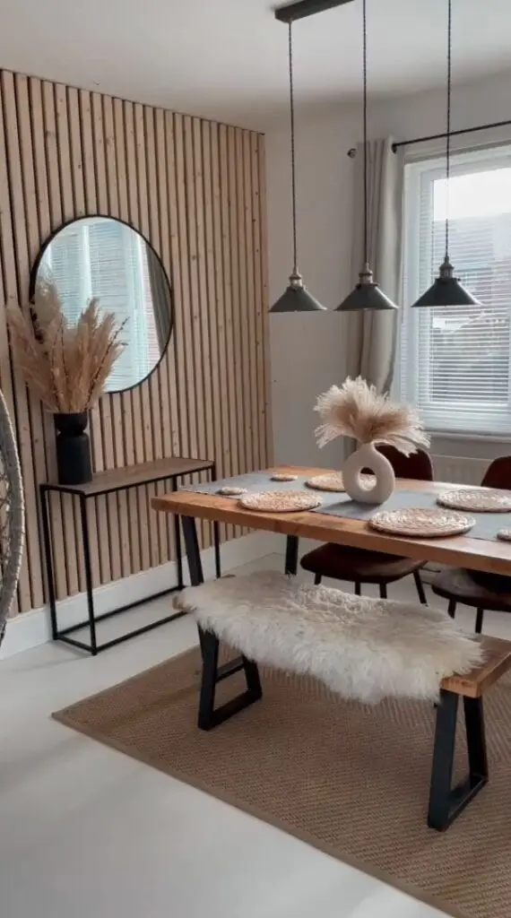 Modern dining room with wooden accents, black pendant lights, and pampas grass centerpiece on a rustic table.