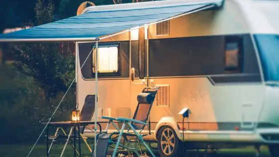 Cozy caravan campsite with canopy, chairs, and lantern at dusk in a tranquil, wooded setting.