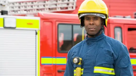 Firefighter in safety gear standing in front of a fire truck, ready for emergency response duty.