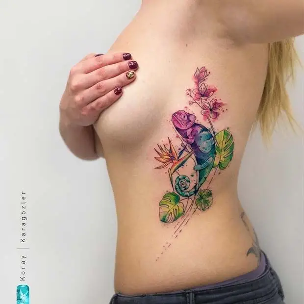 Colorful chameleon tattoo on woman's side with floral accents and vibrant watercolor style.