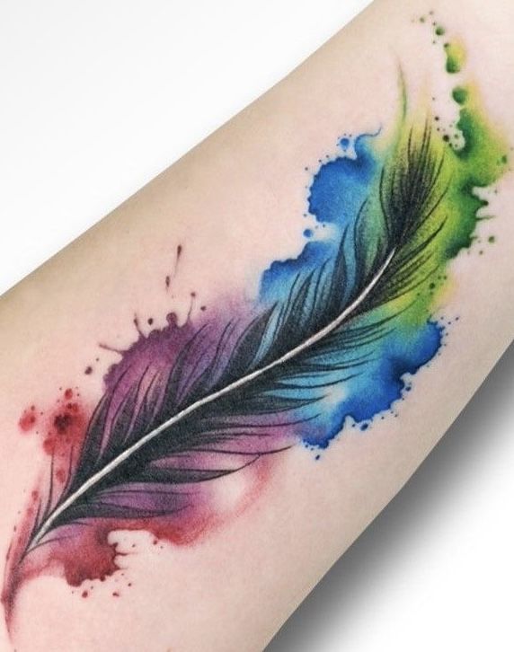 Colorful feather tattoo with vibrant watercolor splashes on forearm, showcasing artistic design and vivid hues.