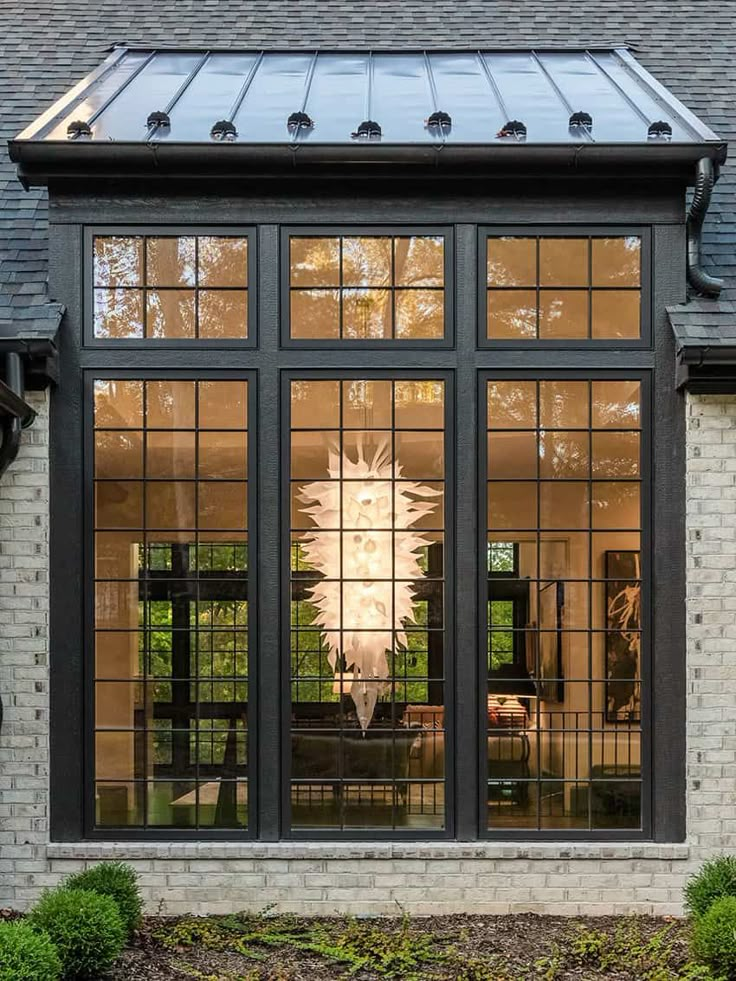 Modern house facade with large windows reflecting trees, showcasing an elegant interior chandelier.