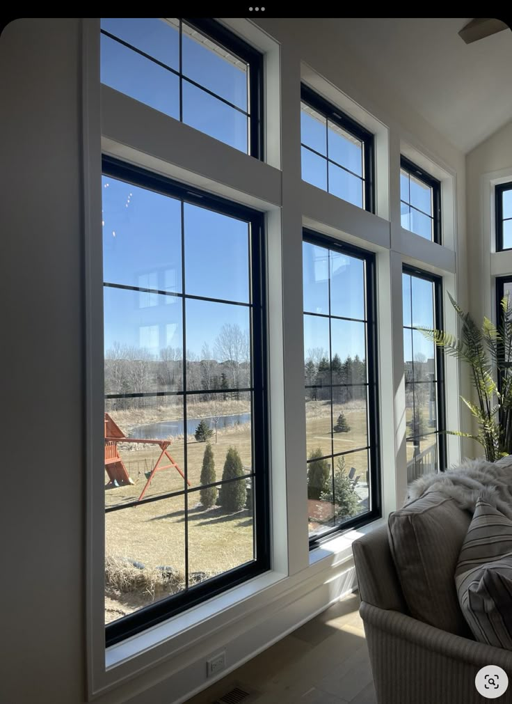 Large windows with black frames, offering a scenic view of a backyard with trees and a blue sky.