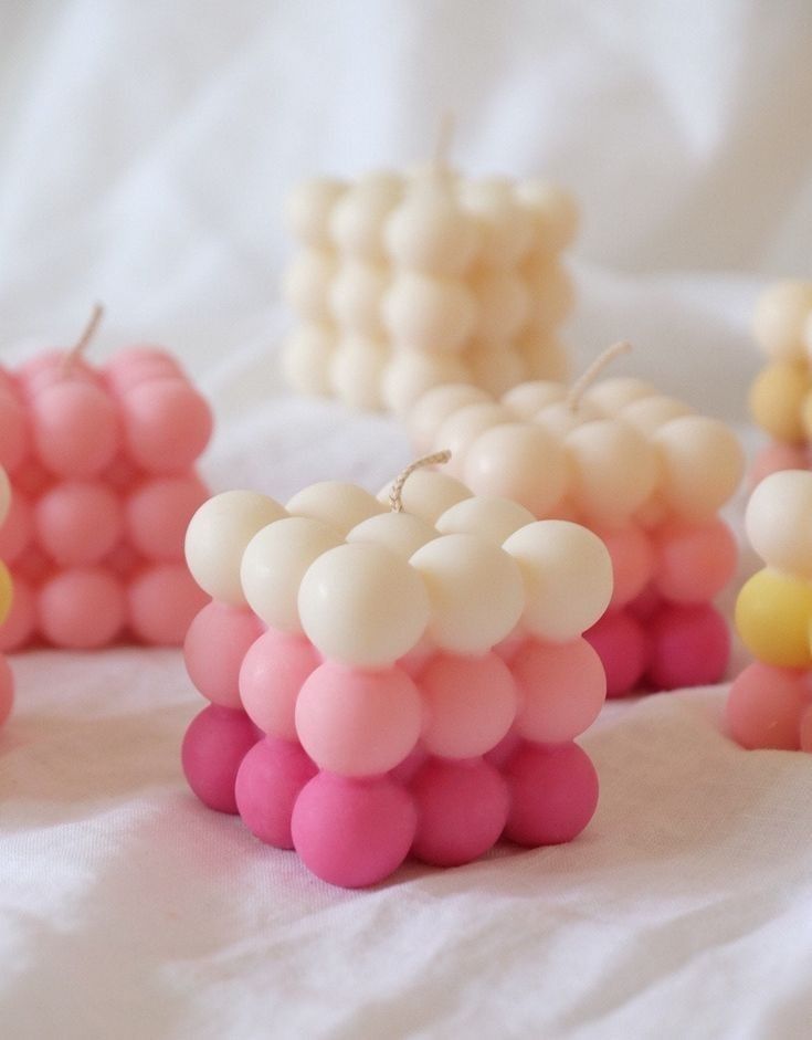 Colorful bubble candles on white fabric, featuring pink and cream hues, create a cozy, decorative ambiance.