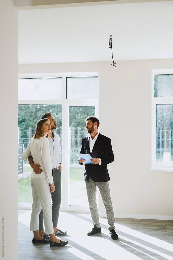 Real estate agent showing new house to interested couple in modern, well-lit living room.