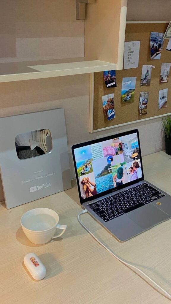 Workspace with a laptop, YouTube silver play button, and corkboard, inspiring creativity and productivity.