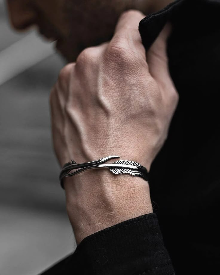 Close-up of a stylish silver feather bracelet on a person's wrist with a black sleeve background.