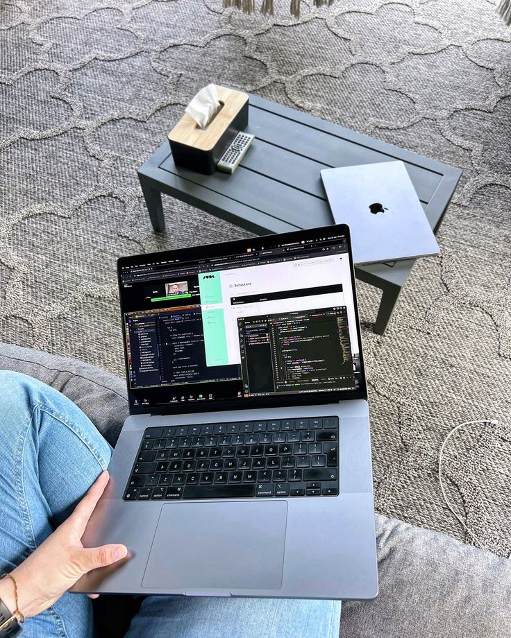 Person programming on a laptop at home patio, another laptop on the table, cozy workspace setup.