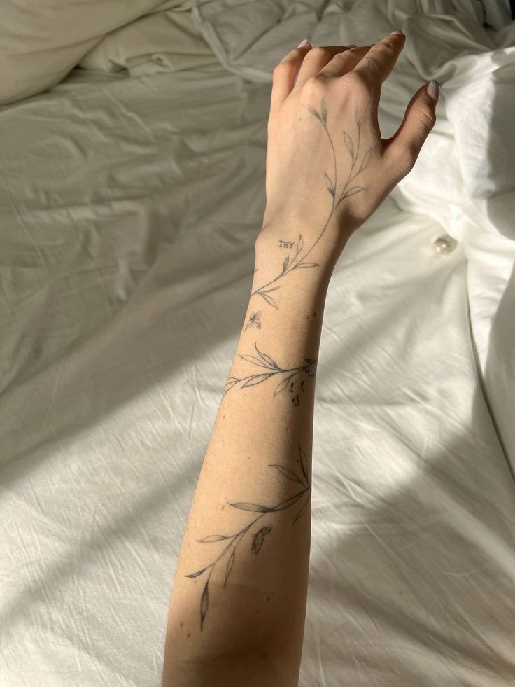 Minimalist floral tattoo on forearm in sunlight against white sheets.