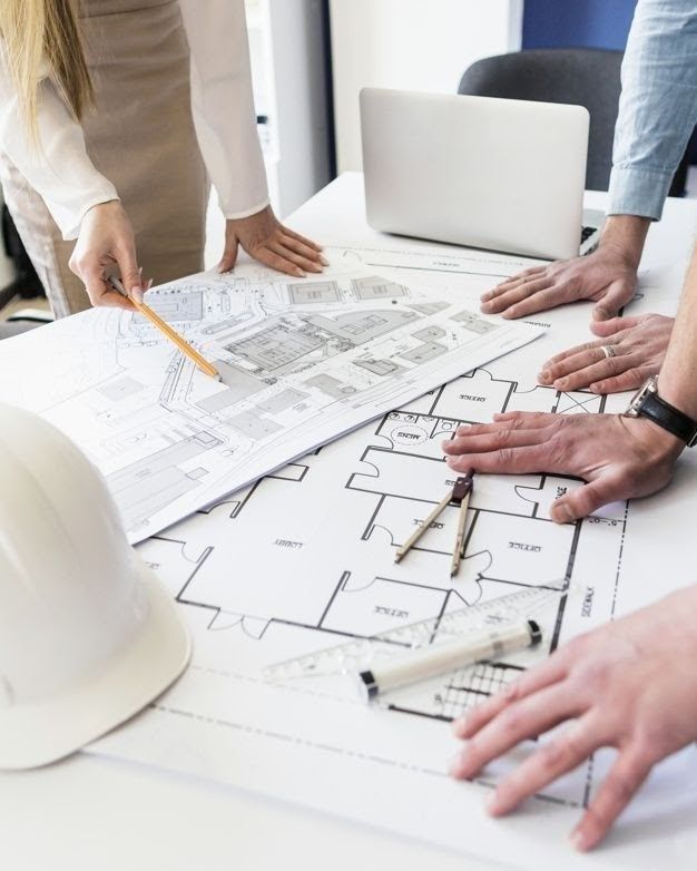 Architects reviewing building blueprints at a desk with tools and a helmet.