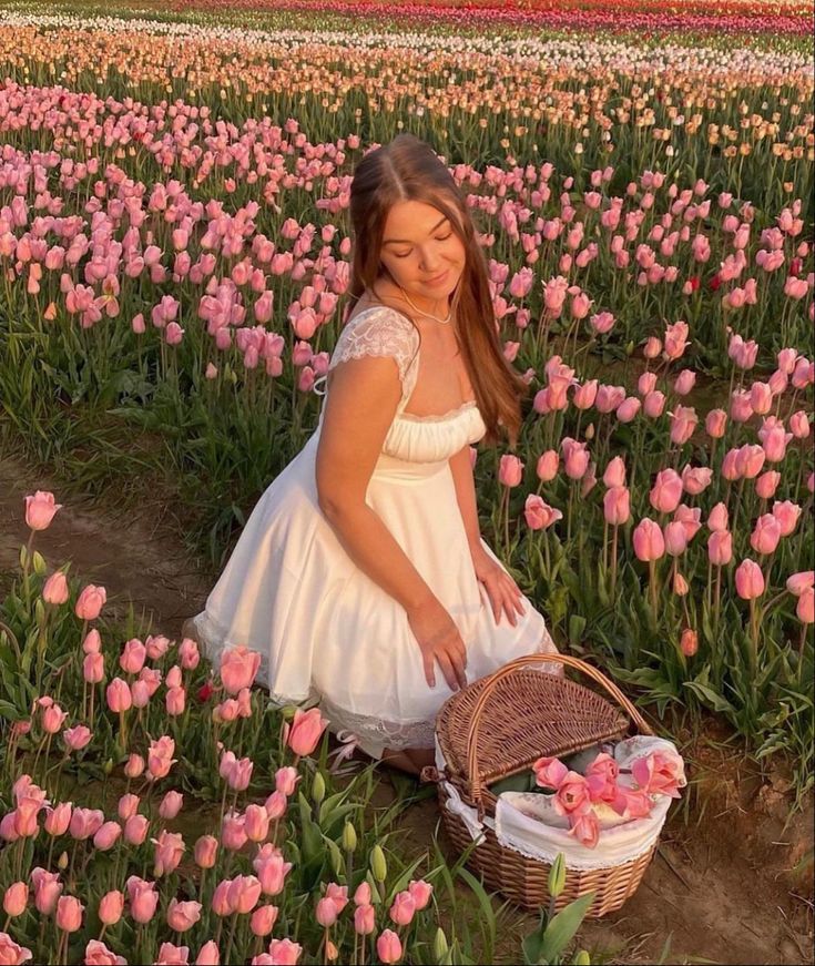 Woman in white dress with picnic basket among pink tulips in a sunset-lit field.