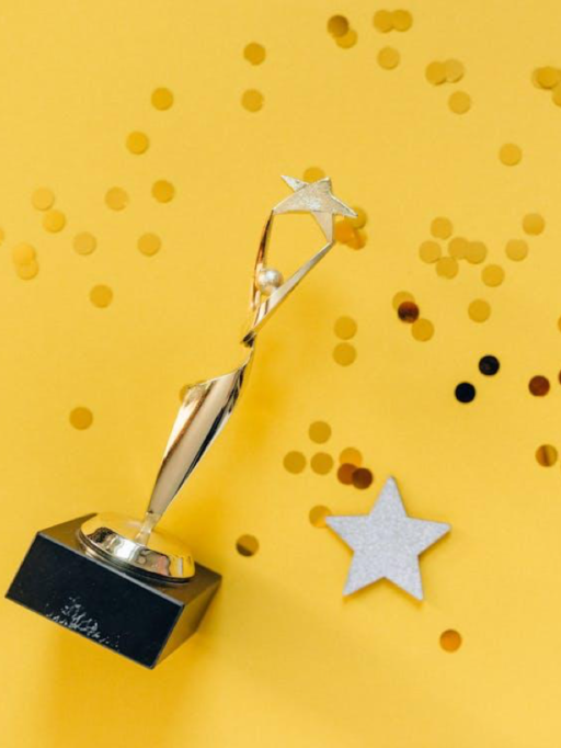 Golden trophy with stars and confetti on a yellow background, celebrating achievement and success.