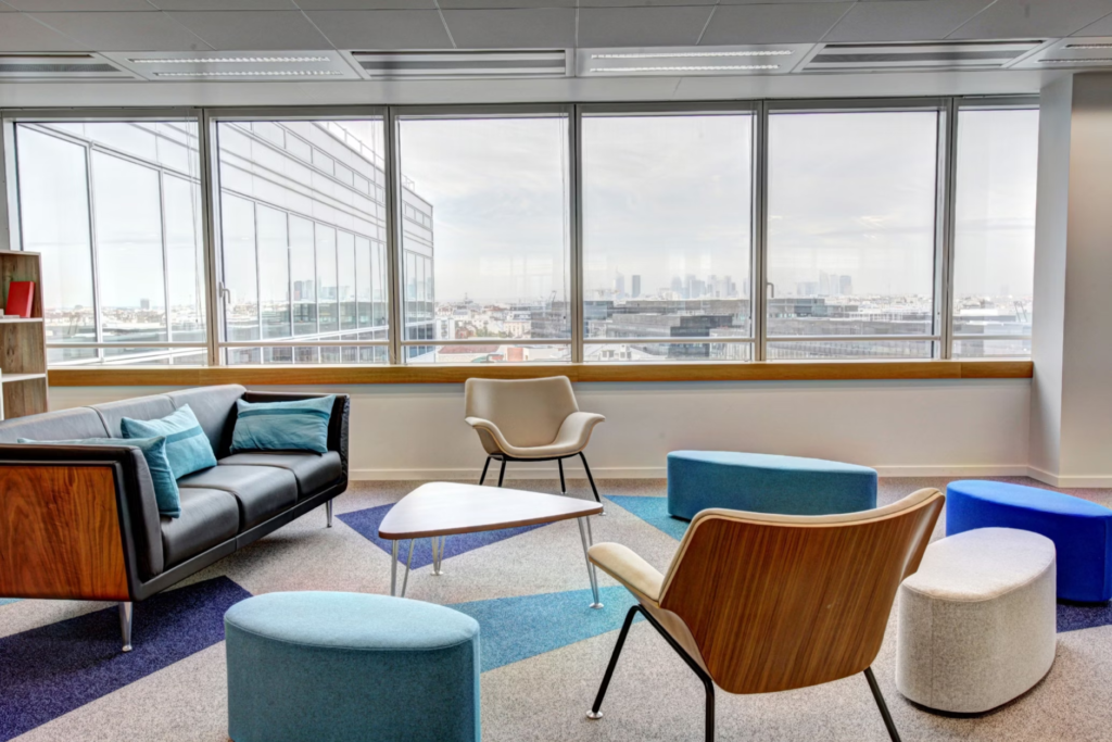 Modern office lounge with panoramic city view, featuring stylish furniture and large windows.