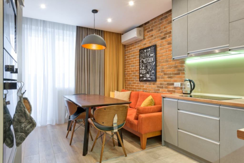 Modern kitchen with wooden table, orange sofa, brick wall, sleek cabinets, and cozy lighting.