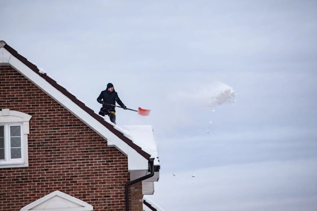 Person shoveling snow off a brick house roof on a winter day.