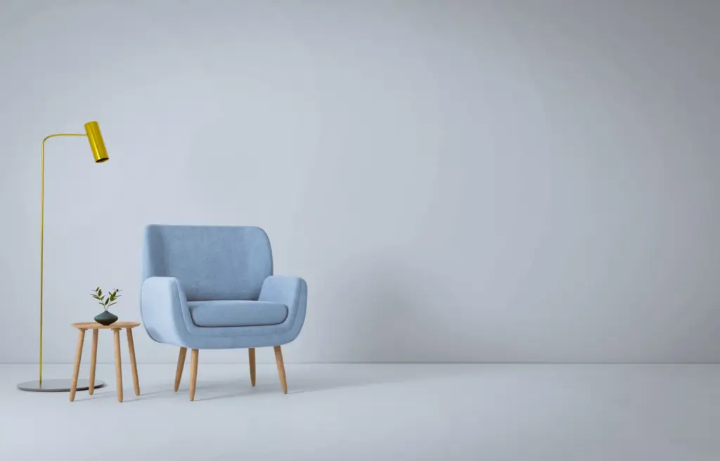 Minimalist room with blue armchair, yellow floor lamp, and small table with plant against a gray wall.