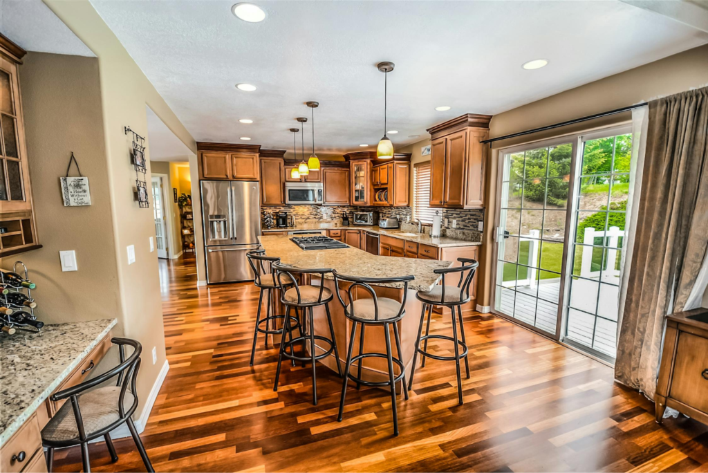 Modern kitchen with wooden cabinets, island, bar stools, stainless steel appliances, and large glass door opening to garden. Hardwood Floors 