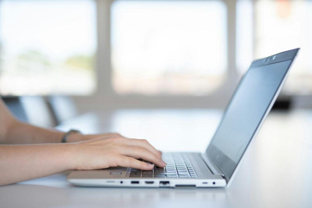 Person typing on a laptop in a bright office setting, focusing on hands and keyboard.