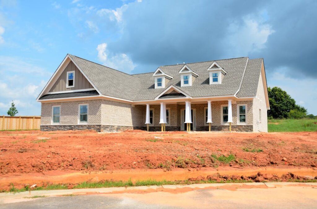 Newly constructed suburban house with gray roof and pillars against a cloudy sky backdrop.