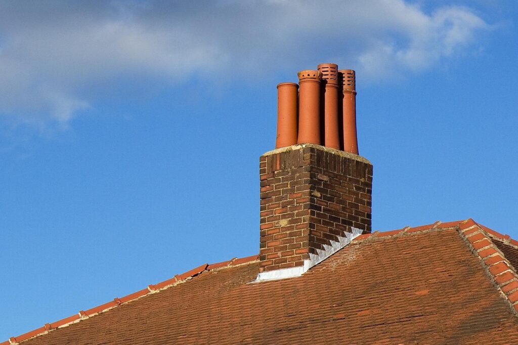 Brick chimney with multiple clay pots on red-tiled roof against blue sky.