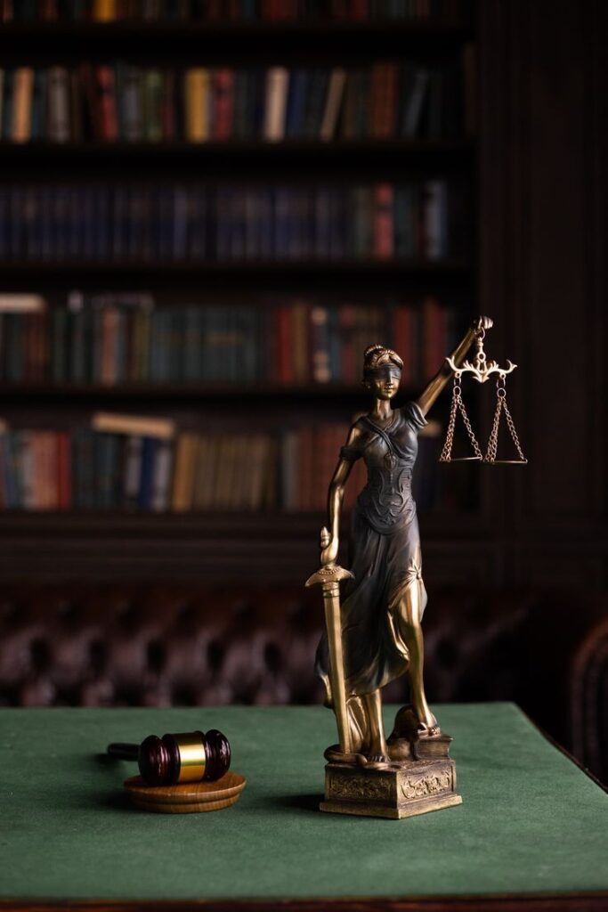 Lady Justice statue with scales and gavel in a library, symbolizing law and justice.