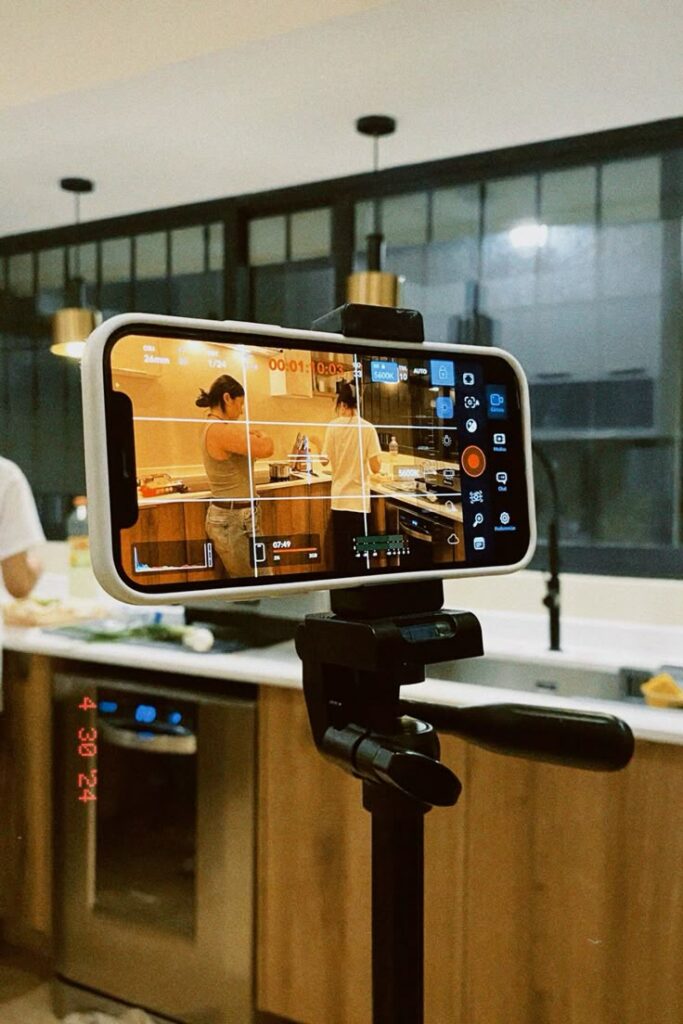 Smartphone on tripod recording a cooking video in a modern kitchen setting.