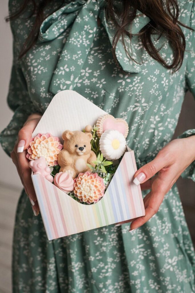 Gift box with teddy bear and floral soaps held by a woman in a floral dress.