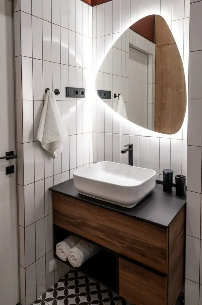 Modern bathroom with illuminated mirror, sleek vanity, white sink, and stylish tiled walls.