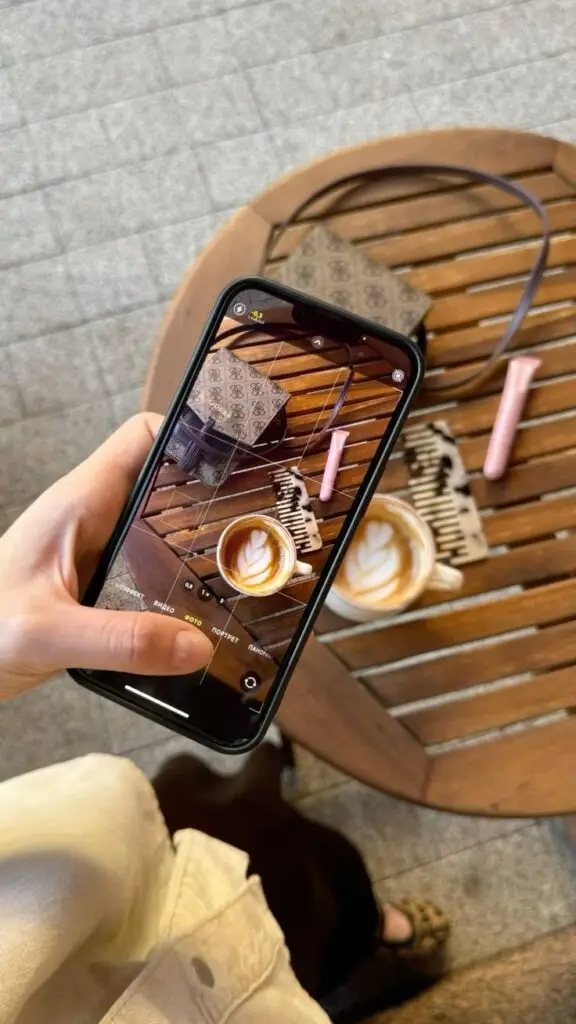 осень идеи фото осень эстетика фото в кофейне идеи идеи для сторис фото в инстаграм Person captures coffee and wallet on wooden table with phone, showcasing aesthetic photography. | Sky Rye Design Person captures coffee and wallet on wooden table with phone, showcasing aesthetic photography.