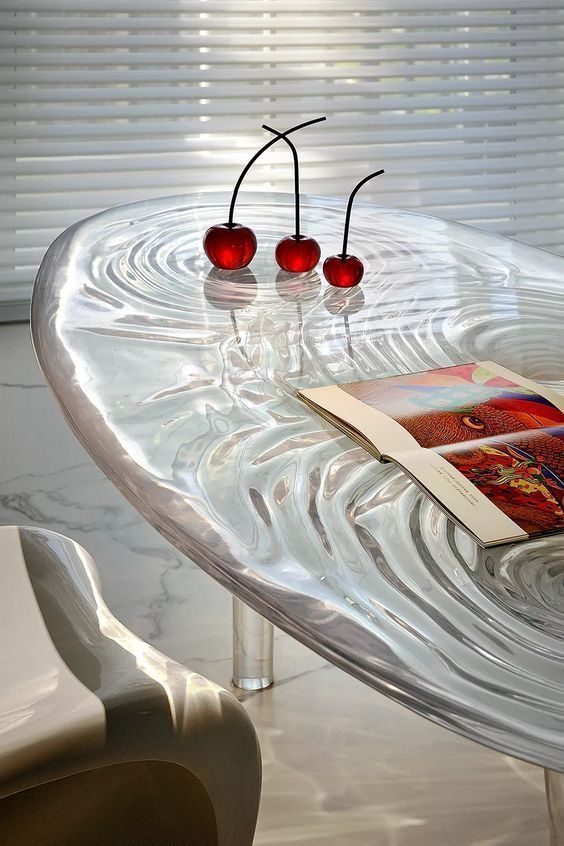 Modern glass table with artistic cherries and open book in bright room with blinds.