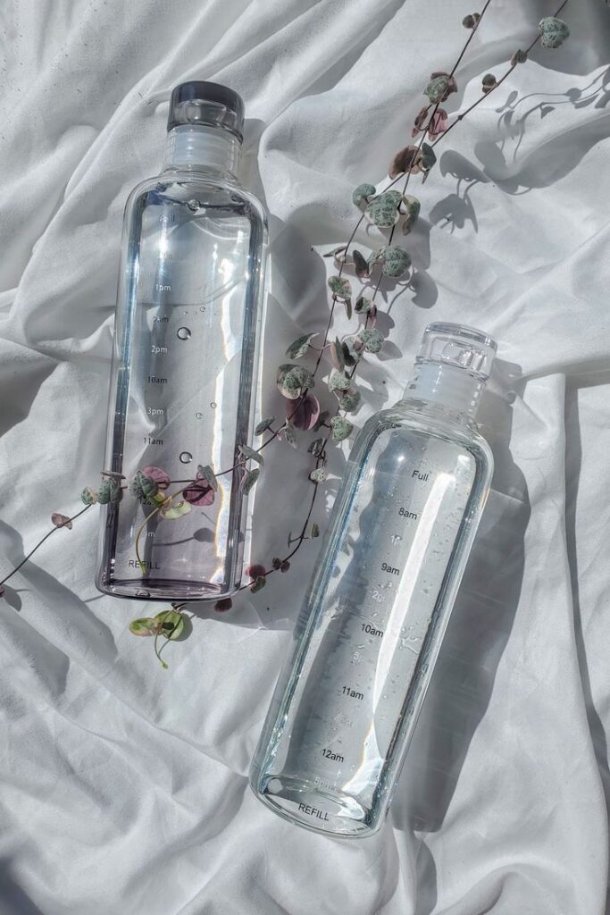 Two clear water bottles with time markers and vines on white fabric background.