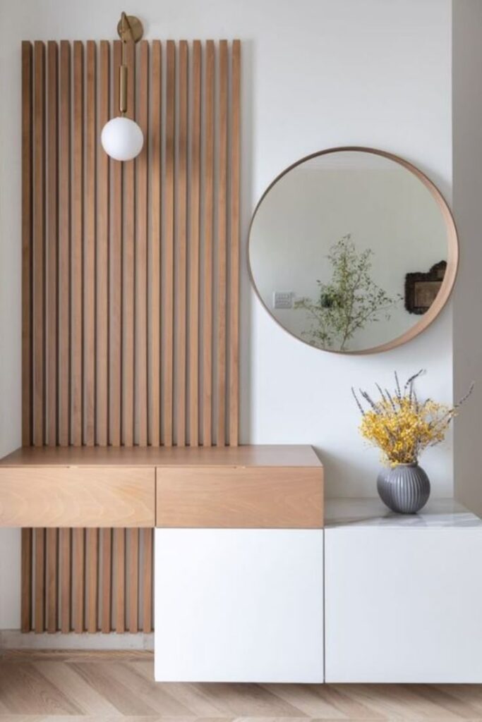 Modern interior design with wood paneling, round mirror, and a vase on a white console for minimalist decor.