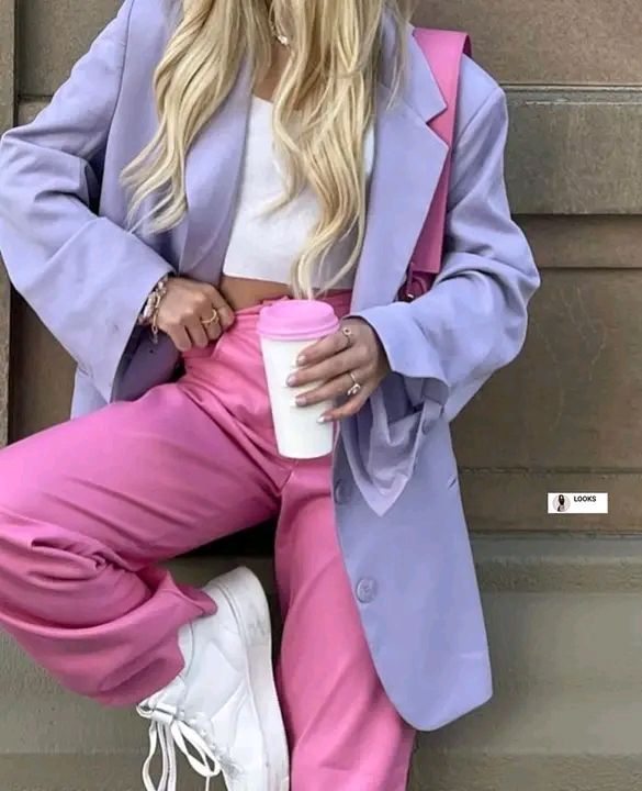 Fashionable woman in lilac blazer and pink pants holding coffee cup, showcasing chic urban street style.