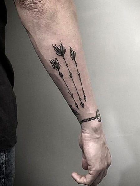 Forearm tattoo featuring three arrows with artistic designs, emphasizing minimalistic and tribal style.