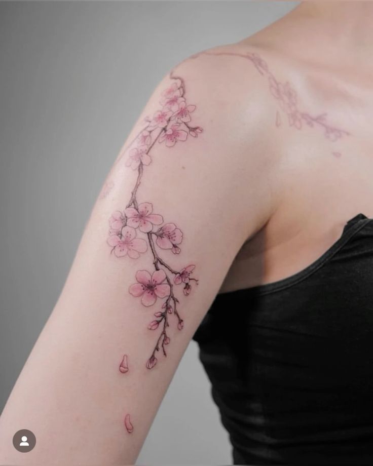 Cherry blossom tattoo on the upper arm, featuring delicate pink flowers and branches.