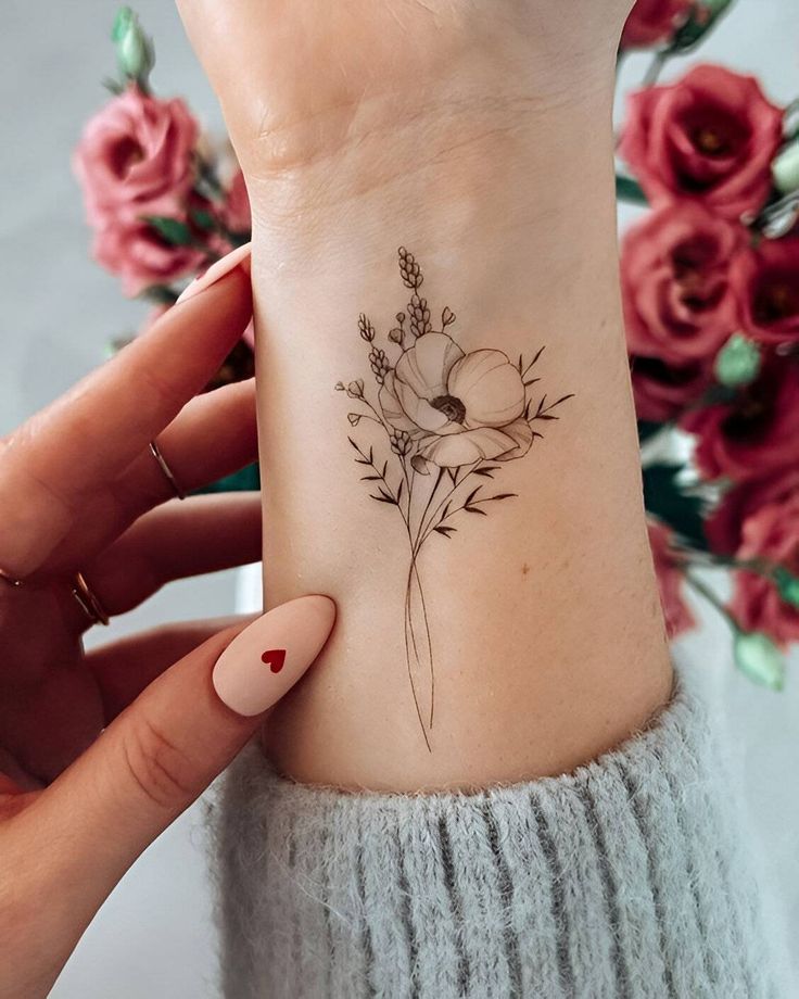 Delicate floral wrist tattoo with an intricate flower design, red roses in the background, and a heart nail art.