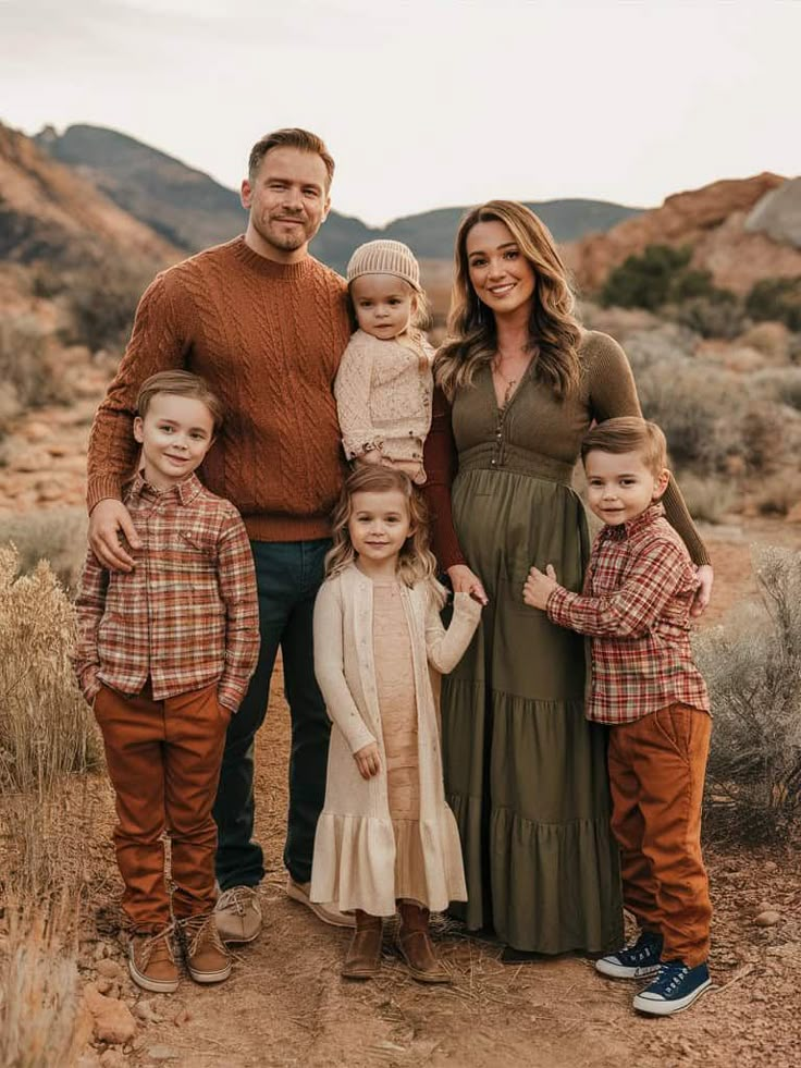 Family posing outdoors in fall attire, surrounded by scenic mountains and dry foliage.