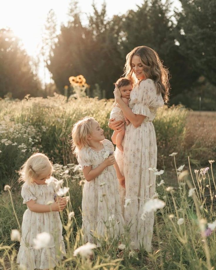 Mother and three daughters in a sunny meadow, wearing matching floral dresses, capturing a serene and joyful moment.