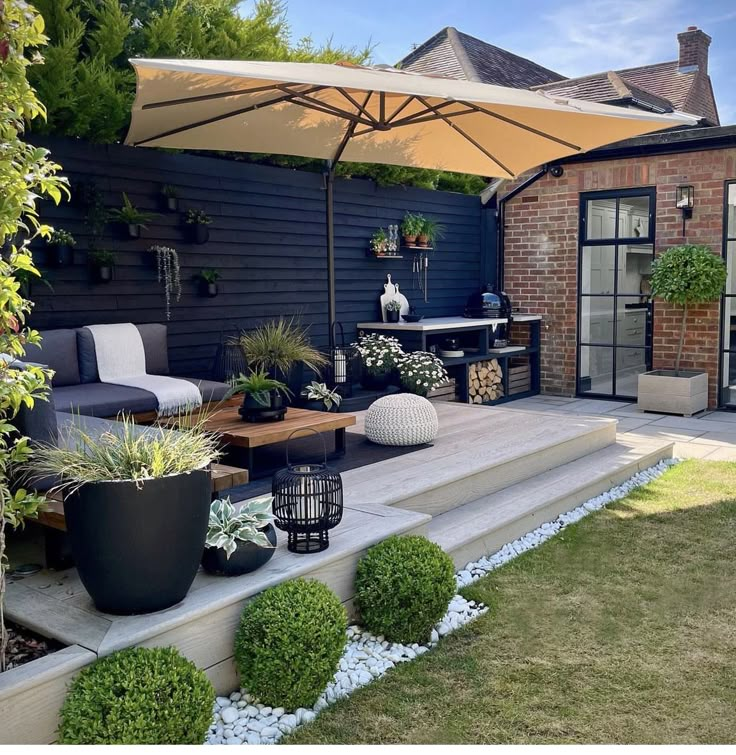 Modern patio with cozy seating, potted plants, and a large umbrella in a brick-walled garden outdoor setting.