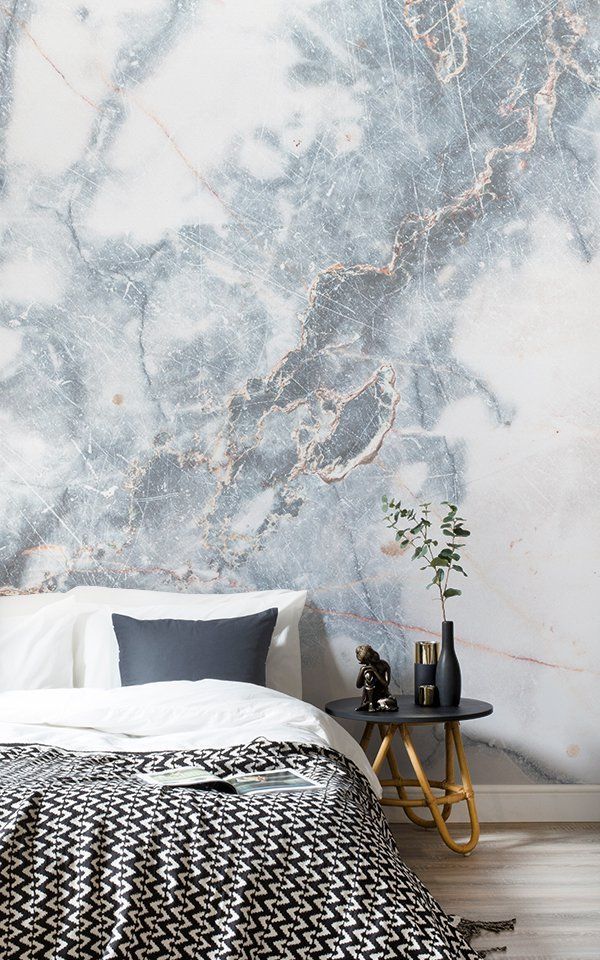 Modern bedroom with marble accent wall, cozy bed, black-and-white blanket, and stylish side table decor.