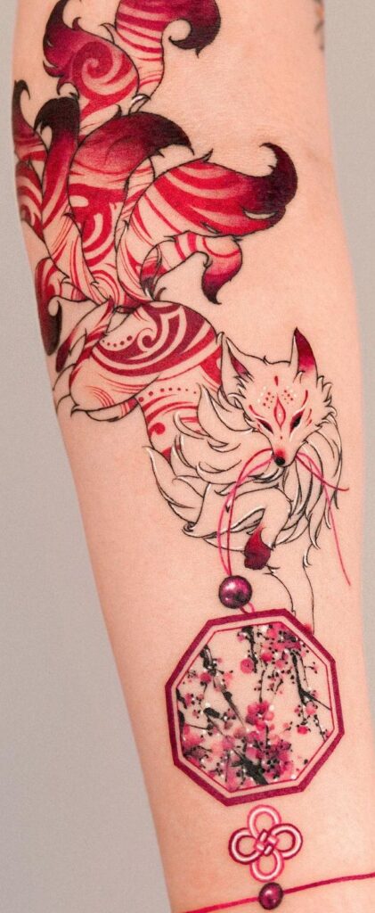 Tattoo of a stylized fox with intricate red patterns and cherry blossom motif on forearm.