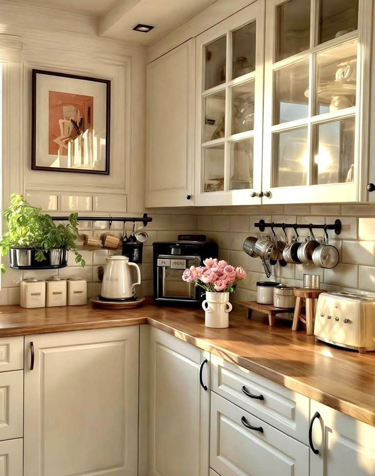 Bright, cozy kitchen with wooden countertops, white cabinets, fresh herbs, and a bouquet of pink flowers.