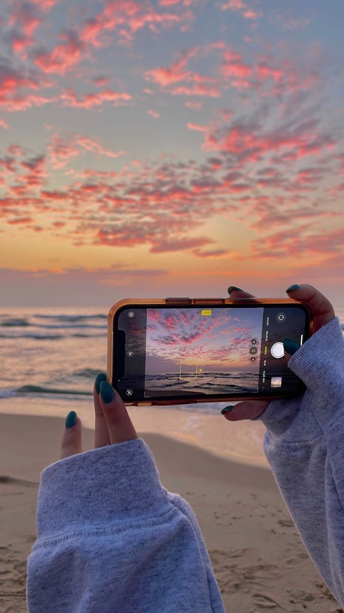 Person captures stunning sunset over ocean on smartphone, pink clouds contrasting the serene sea view.