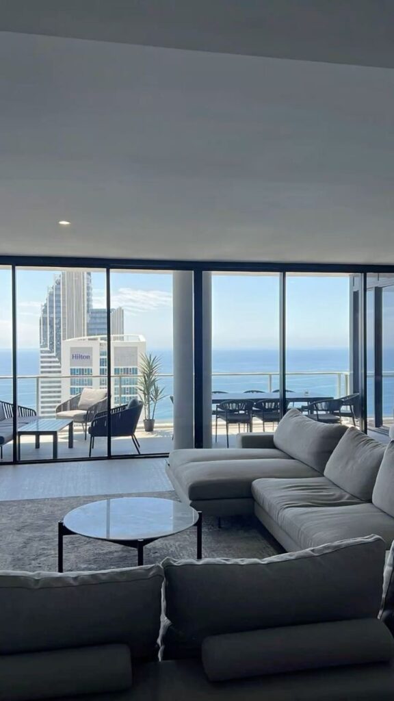Modern living room with ocean view, glass walls, and sleek furniture in luxury high-rise apartment.