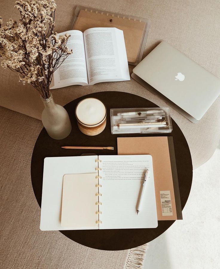 Cozy workspace with a laptop, books, open notebook, pen, dried flowers, and coffee on a round table. Perfect for studying.